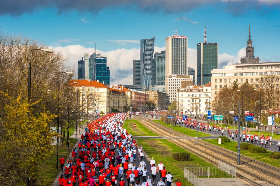 zdjęcie przedstawia wielotysięczną grupę zawodników ubranych w białe i czerwone koszulki biegnących aleją Niepodlełości w Warszawie