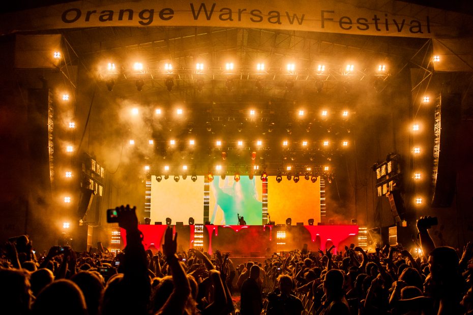 Zdjęcie przedstawia scenę i koncert na festiwalu muzycznym Orange Warsaw Festival, przed sceną zgromadzony jest tłum fanów z rękami w górze