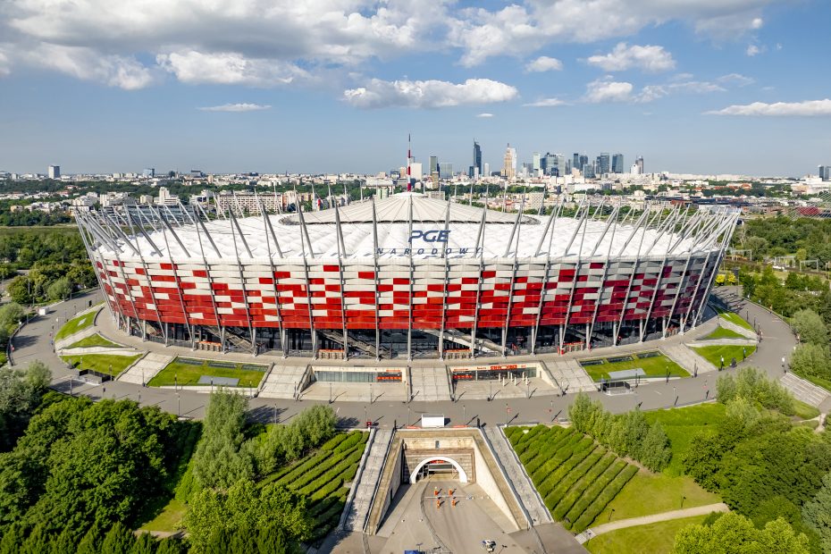 Zdjęcie przedstawia stadion PGE Narodowy latem, w tle widoczna panorama centrum Warszawy