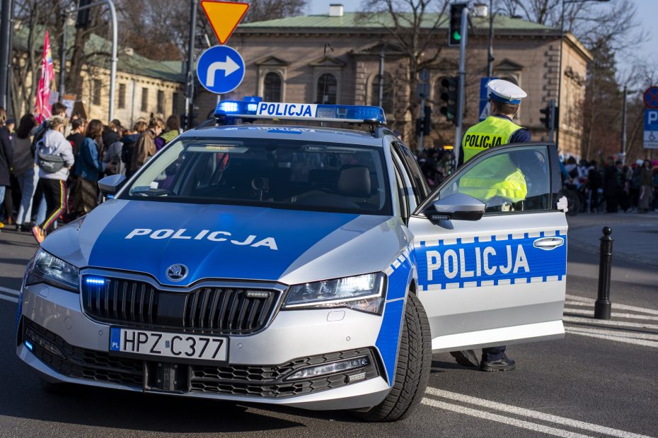 zdjęcie przedstawia policyjny radiowóz stojący na środku skrzyżowania z którego wysiada umundurowany funkcjonariusz drogówki