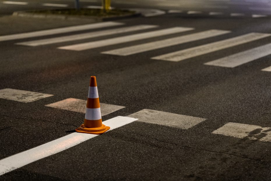 zdjęcie przedstawia namalowane na jezdni przejście dla pieszych. Na pierwszym planie jest świeżo namalowana linia separacyjna. Na jej końcu stoi stożek drogowy.