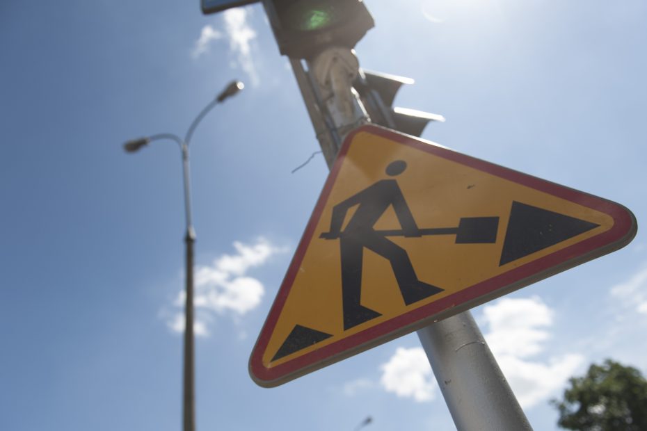 znak drogowy "uwaga! roboty drogowe" zawieszony na latarni