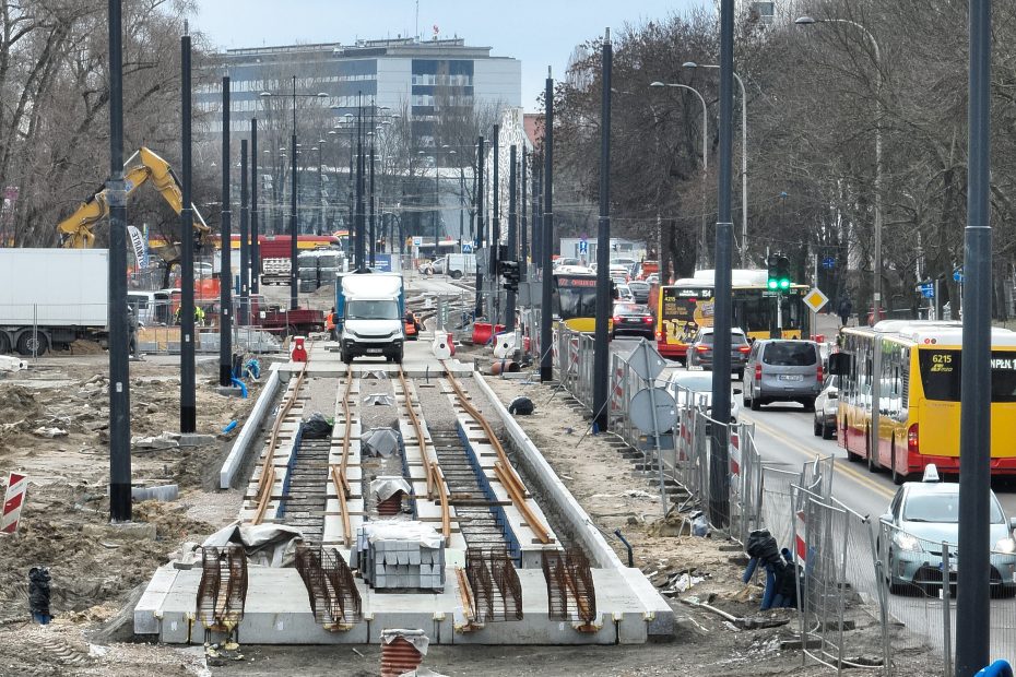 Plac budowy na Bitwy Warszawskiej 1920 r. Stoją nowe słupy latarni, podkłady pod tory tramwajowe, sprzęt budowlany. Po prawej stronie od budowy - sznur samochodów