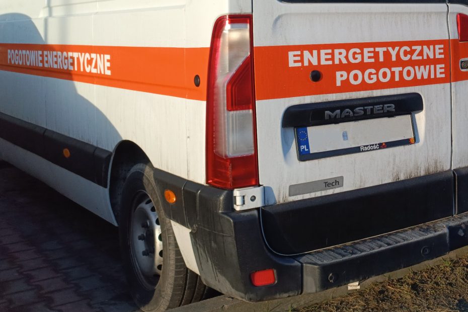 Zdjęcie przedstawia tylny narożnik białej furgonetki z pomarańczowymi pasami po bokach z napisami "pogotowie energetyczne".