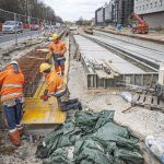 Zdjęcie pokazuje prace przy budowanym torowisku na ulicy Bitwy Warszawskiej 1920 r. Na pierwszym planie widoczni są robotnicy w odzieży ochronnej i kaskach. Obok widać szyny.