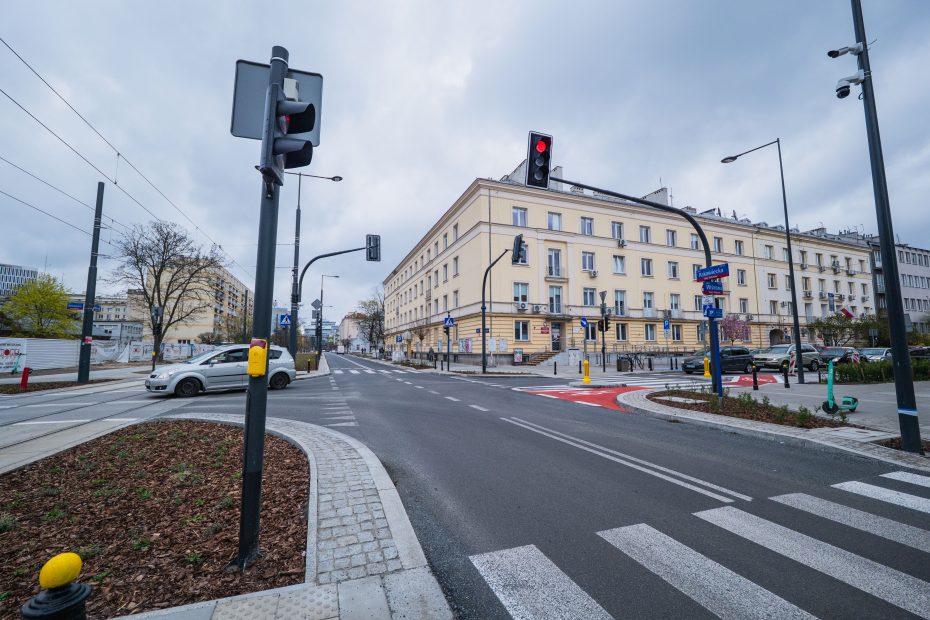 Zdjęcie przedstawia skrzyżowanie ulic Rakowieckiej i Wiśniowej. Na pierwszym planie widoczna jezdnia, pasy dla pieszych i jadący samochód. W tle mokotowski ratusz.