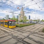 Zdjęcie przedstawia tramwaj przejeżdżający przez Rondo Dmowskiego. Na pierwszym planie widać krzyżujące się szyny i tramwaj, a w tle - Pałac Kultury i Nauki.