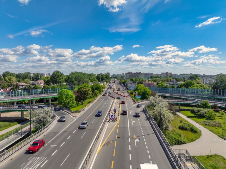 Zdjęcie przedstawia nowo wybudowane wiadukty Trasy Łazienkowskiej nad Saką Kępą. Fotografia została wykonana na węźle z ulicą Wał Miedzeszyński w kierunku Saskiej w słoneczny, letni dzień.