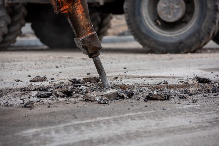 Zdjęcie przedstawia prace drogowe. Widoczny młot pneumatyczny kruszący nawierzchnię jezdni.