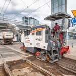 Zdjęcie przedstawia maszynę budowlaną pracującą na torowisku tramwajowym w Alejach Jerozolimskich przy Rondzie Czterdziestolatka.