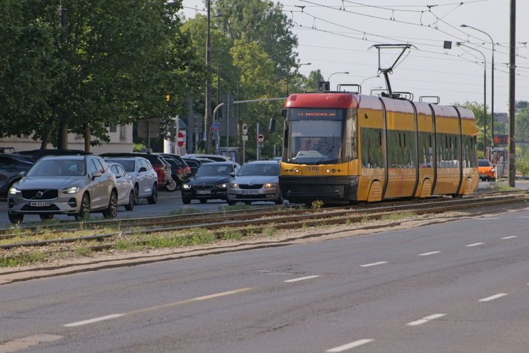 Zdjęcie przedstawia tramwaj jadący po szynach w Alei Niepodległości na wysokości ulicy Filtrowej. W tle widoczne są samochody jadące do centrum.