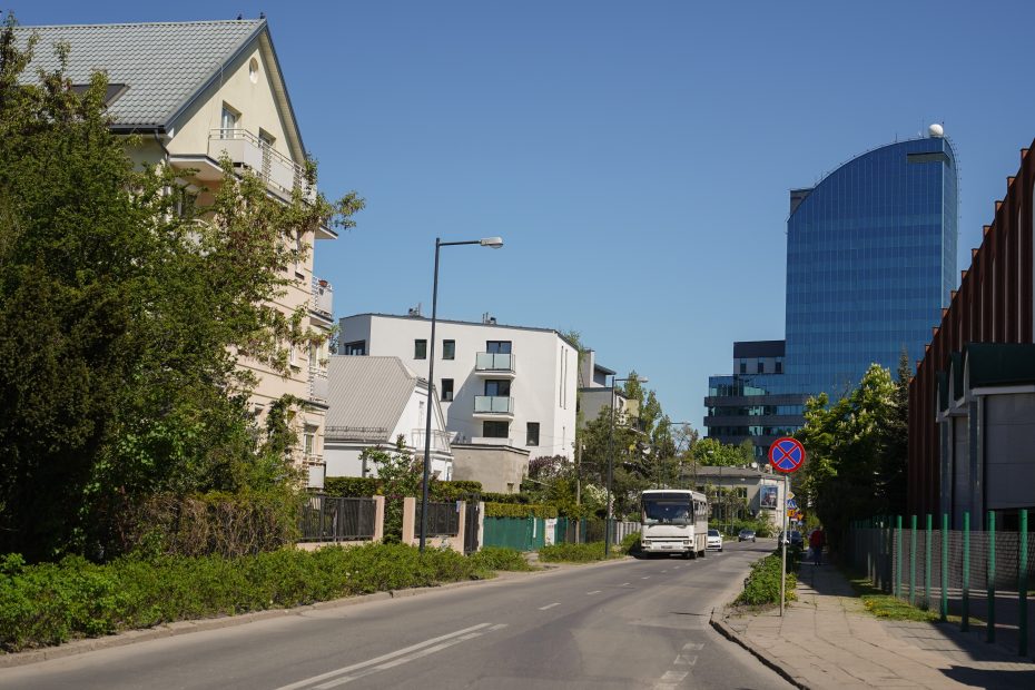 Zdjęcie przedstawia ulicę Spalinową na Pradze-Południe. Po lewej stronie widoczna niska zabudowa - jedno i wielorodzinna - a w tle biurowiec. Po prawej stronie widać też fragment fasady kościoła. Jednojezdniową ulicą jedzie autokar i dwa samochody osobowe.